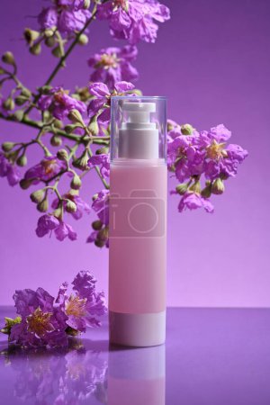Markenlose rosafarbene Pumpflasche mit mehreren lila Blüten auf hellviolettem Hintergrund. Das Konzept der Creme, Lotion, Feuchtigkeitscreme Produkte Attrappe