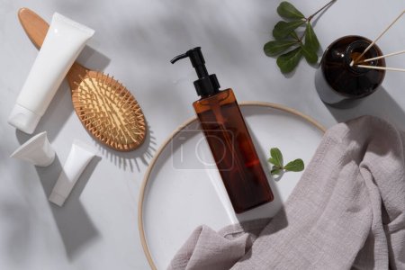 An empty label pump bottle putted on a round dish, tubes with different sizes, a wooden brush and reed diffusers displayed. Skincare product concept