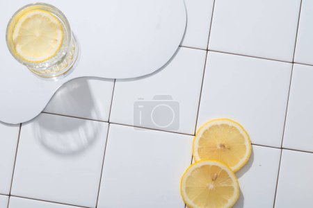 Téléchargez les photos : Miroir géométrique avec un verre de tranche de citron posé sur un fond de mosaïque blanche. Citron (Citrus limon) contient beaucoup de potassium pour aider à stimuler l'activité cérébrale. Espace vide - en image libre de droit