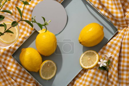 Ein pastellfarbenes Tablett mit Zitronen, einem runden Spiegel und einem leeren Raum, um Ihr Schönheitsprodukt aus Zitronenextrakt auszustellen. Zitrone (Citrus limon) ist gut für Haut, Gesundheit und Haare