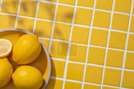 Téléchargez les photos : Un plat rond de citrons isolés sur fond de carreaux de mosaïque jaune avec des feuilles tropicales ombre. Citron (Citrus limon) peut aider à diminuer l'inflammation et l'huile dans votre peau. Espace de copie - en image libre de droit