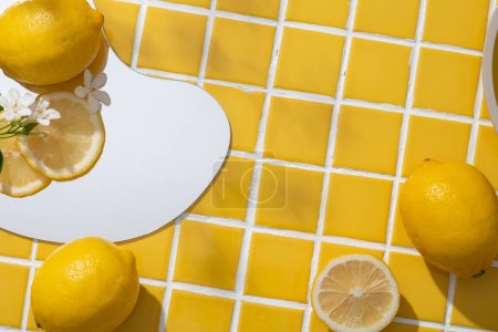 Téléchargez les photos : Miroir géométrique avec des tranches de citron et de petites fleurs blanches affichées sur. Espace vide sur fond de carreaux de mosaïque jaune pour montrer votre produit cosmétique naturel d'extrait de citron (Citrus limon) - en image libre de droit