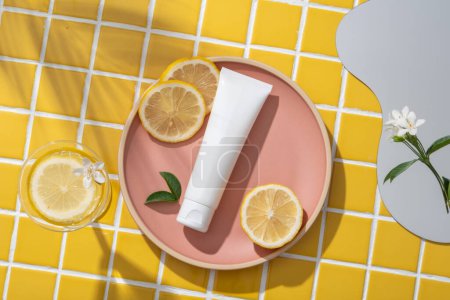 Some Lemon slices and a white tube put on a pink dish. A mirror, white flowers and a glass are displayed. Shadow of tropical leaves. Lemon (Citrus limon) is a popular fruit for its vitamin C content