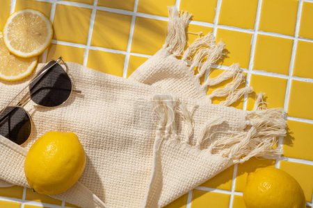 Téléchargez les photos : Tranches de citron, lunettes de soleil et un foulard en laine disposés sur fond de carreaux de mosaïque jaune. Citron (Citrus limon) peut aider à améliorer le système immunitaire. Vue du dessus - en image libre de droit