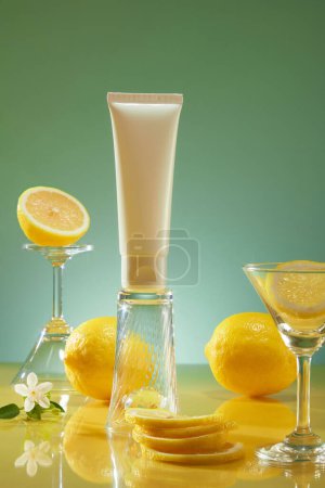 Téléchargez les photos : Étiquette vierge tube blanc debout sur un verre à l'envers, arrangé avec plusieurs tranches de citron, fleurs et verres. Citron (Citrus limon) est considéré comme un ingrédient végétalien - en image libre de droit