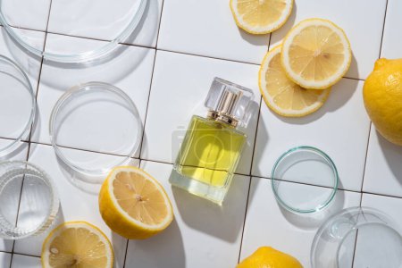 Foto de Frasco de vidrio transparente de perfume extraído del aceite esencial de limón arreglado con placas de Petri y rodajas de limón. Limón (Citrus limon) se puede utilizar en la producción de perfumes - Imagen libre de derechos