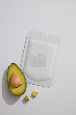 Half of an avocado decorated with a mask sheet with empty label for branding mockup. Face mask extracted from Avocado (Persea americana) can treat acne and moisturize the skin