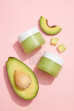 Photo for Avocado slices arranged with two unlabeled jars on light pink background for product promotion of Avocado (Persea americana) extract. It helps strengthen nails and hair - Royalty Free Image