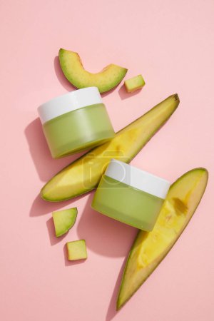 Photo for Top view of green jars without label decorated with Avocado slices against pastel pink background. Avocado (Persea americana) can ease your sunburned skin. Branding mockup of Avocado extract - Royalty Free Image