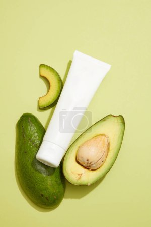 Photo for Two halves of an avocado decorated on pastel background with an unlabeled tube for cosmetic presentation of Avocado extract. Avocado (Persea americana) has many benefits for skin and hair - Royalty Free Image
