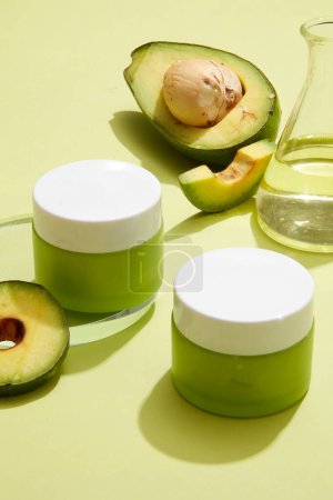 Green jars without label displayed with Avocado essential oil contained inside an erlenmeyer flask. Avocado (Persea americana) is an ingredient that is useful for skin beauty