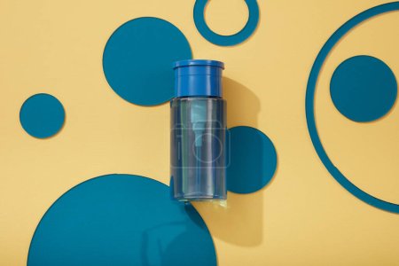 A push down pump dispenser bottle with empty label placed on pastel background with many blue acrylic sheets in round shape. Beauty product mockup