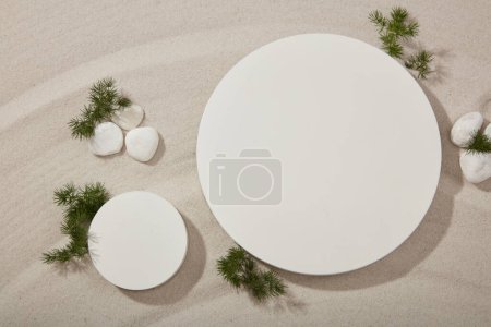 Two round podiums in white color decorated with several gravels and green leaves. Modern minimal showcase scene for cosmetic products promotion