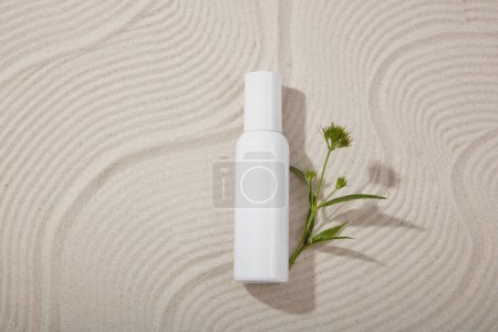 Foto de Botella cosmética sin marca decorada con una rama de flores sobre un fondo arenoso con patrón de ondas. Cosmética de belleza orgánica natural concepto - Imagen libre de derechos