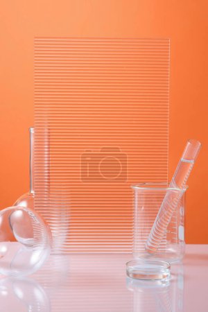 Photo for A glass petri dish, a beaker with a test tube of liquid inside and a ribbed acrylic sheets are decorated on orange background. Research content - Royalty Free Image