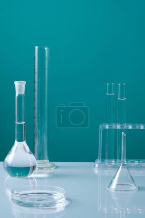 Foto de Una placa de Petri de vidrio llena de líquido decorado con tubos de ensayo y muchos artículos de vidrio de laboratorio. Fondo azul mínimo. Espacio vacío en el medio para la presentación del producto - Imagen libre de derechos