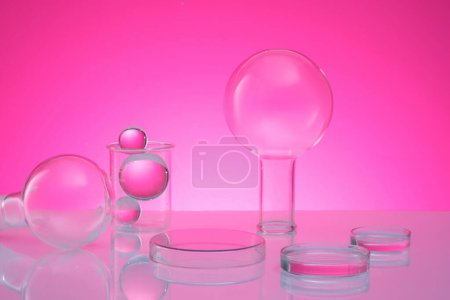 Téléchargez les photos : Un bécher avec quelques boules de verre à l'intérieur décoré d'un podium rond transparent vide sur fond rose. Espace vide pour afficher des produits cosmétiques - en image libre de droit