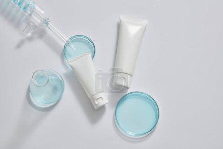 Photo for Two white tubes with different sizes decorated with petri dishes containing blue liquid, a spiral pipe tube and an erlenmeyer flask. Cosmetic product mockup - Royalty Free Image