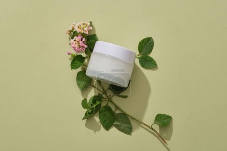 Téléchargez les photos : Un pot cosmétique blanc sans étiquette affichée avec des fleurs de camara Lantana. Emballage de récipient de marque de soins de la peau avec extrait de fleurs de camara Lantana - en image libre de droit