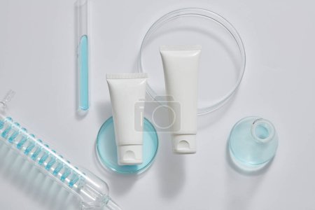 Laboratory concept with test tubes, petri dish and an erlenmeyer flask filled with blue fluid, displayed with empty label tube. Cosmetic packaging mockup