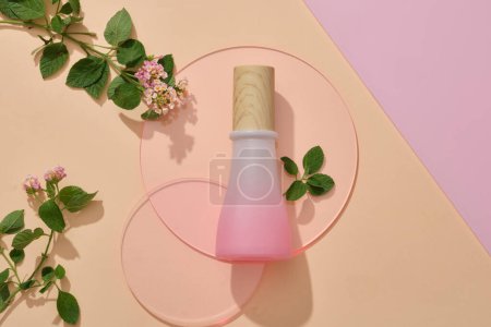 Foto de Un frasco de color rosa con tapa de madera colocada en hojas de acrílico redondas de color rosa con flores de Lantana camara. Maqueta de productos de marca, diseño de envases para productos de cuidado de la piel de belleza - Imagen libre de derechos