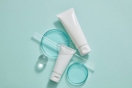 Two white tube with different sizes arranged with petri dishes, a glass rod and a transparent ball on pastel blue background. Beauty product mockup with empty label