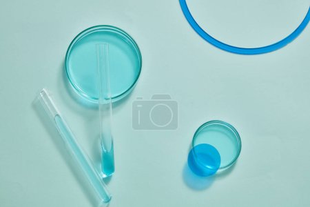 Foto de Sobre un fondo azul claro, se muestran placas de Petri y tubos de ensayo llenos de líquido azul. El espacio en blanco se puede utilizar para mostrar el producto cosmético - Imagen libre de derechos