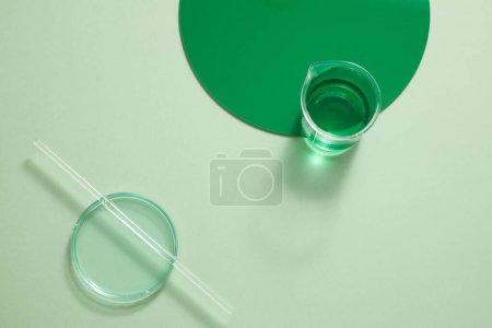 Foto de Un vaso de precipitados que contiene líquido verde decorado con un tablero de plástico verde redondo y una varilla de vidrio colocada encima de una placa de Petri. Espacio vacío para la promoción de productos. espacio de copia - Imagen libre de derechos