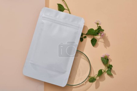 Photo for Unlabeled facial mask sheet decorated with a glass petri dish and some Lantana camara flowers. Beauty branding promotion with natural concept - Royalty Free Image