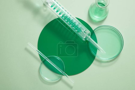 Photo for Petri dishes, test tube with spiral pipe and an erlenmeyer flask filled with green fluid. Vacant space on the plastic board to show your product - Royalty Free Image