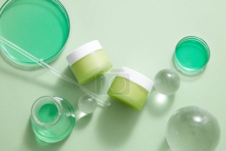 Photo for Two unlabeled jar placed on white background with some glass balls, green liquid contained in petri dishes and erlenmeyer flask. Mockup of skin care or body care product - Royalty Free Image