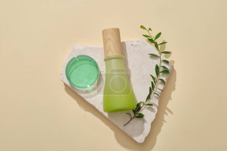 Unbranded white and green gradient color jar placed on a stone podium with fern and a glass petri dish of green liquid. Empty label for cosmetic product mockup