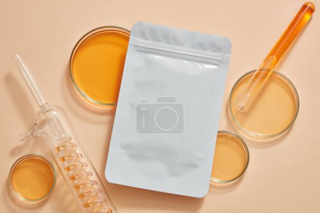 Photo for A mask sheet with unlabeled packaging decorated with petri dishes and test tube of orange liquid. Natural organic beauty cosmetics concept. Research content. Branding mockup - Royalty Free Image