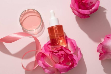 Téléchargez les photos : Concept naturel de soin de la peau avec un liquide rose extrait de Rose (Rosa) contenu dans une boîte de Pétri en verre et une bouteille en verre avec compte-gouttes. Modèle de marque - en image libre de droit