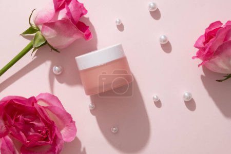 Pearls are scattered over white background with an empty label pink jar. Rose (Rosa) can help to reduce the appearance of redness and swelling