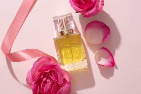 Transparente Glasflasche mit Parfüm und Rosenblättern. Ätherisches Öl, das aus der Rose (Rosa) gewonnen wird, kann zur Herstellung von Parfüm verwendet werden. Leeres Etikett für Produkt-Attrappe