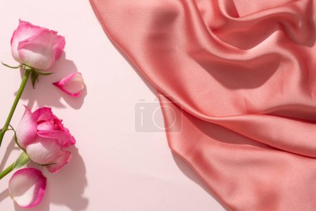 Rosen auf weißem Hintergrund mit einem luxuriösen rosa Stoff dekoriert. Leerraum in der Mitte für kosmetische Produktwerbung für Rosenextrakt