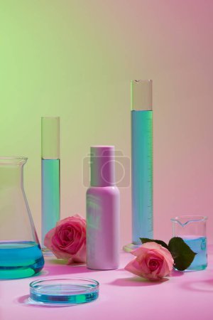 Flasche mit leerem Etikett, dekoriert mit Laborgläsern aus blauer Flüssigkeit und Rosen. Mockup-Flasche für die Hautpflege Kosmetik aus Rose extrahiert (Rosa)