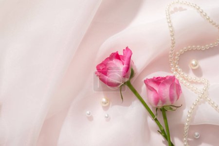 Against a white chiffon fabric background, Roses are decorated with pearls and pearl necklace. Rose (Rosa) essential oil has many beneficial properties