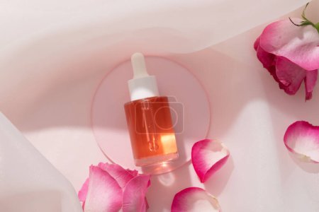 Photo for Round acrylic sheet with an empty label dropper bottle of pink liquid placed on with some Rose petals. Rose (Rosa) essential oil can help to control skin texture - Royalty Free Image