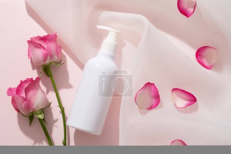 Photo for White pump bottle dispenser without label placed on chiffon fabric with Rose petals. Roses (Rosa) have anti-inflammatory and antibacterial properties - Royalty Free Image