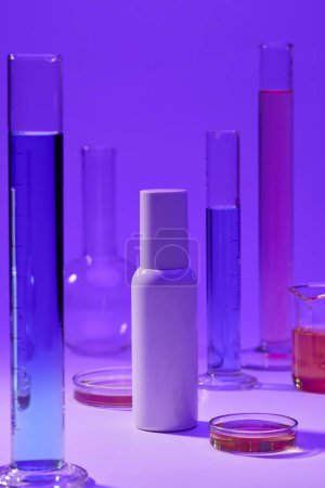 Foto de Líquido con color azul y rosa contenido en el interior cilindro de medición, vaso de precipitados y placa petri. Botella sin marca para maqueta - Imagen libre de derechos