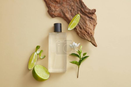 Draufsicht auf eine transparente Nebelsprühflasche mit Limettenscheiben (Citrus aurantiifolia) und einem Blütenzweig. Mockup für Parfüm-Duftprodukt. Markenförderung