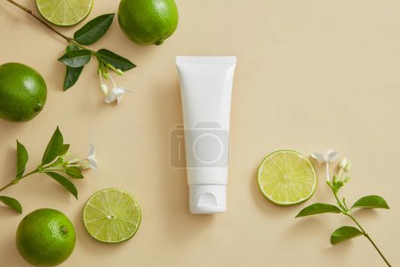 A white tube without label put in the middle with flower branches and Limes displayed around. Lime (Citrus aurantiifolia) has many benefits for skin and hair