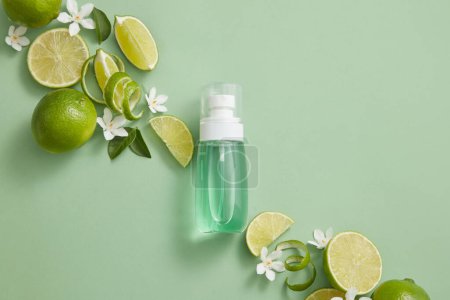 Photo for A transparent bottle containing blue liquid inside is displayed with white flowers, leaves, Lime peels and slices. Lime (Citrus aurantiifolia) helps skin look smoother and more vibrant - Royalty Free Image