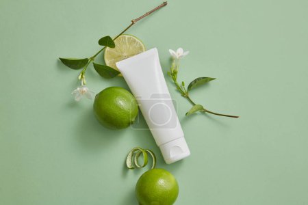 Top view of a white tube with empty label decorated with some Limes and white flower branches. Lime (Citrus aurantiifolia) is used in production of cosmetic as ingredient