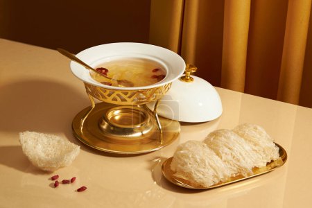 Eine goldene Schüssel mit essbarem Vogelnest aufgesetzt, ein paar getrocknete Goji-Beeren und Vogelnestsuppe mit Jujube, die in einem Futterwärmer enthalten ist. Vogelnest ist eine seltene traditionelle Medizin
