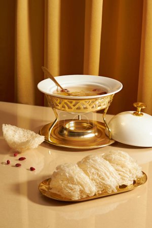 Vogelnestsuppe, die in einem Futterwärmer mit einem Löffel enthalten ist, eine goldene Schüssel essbaren Vogelnestes, die mit getrockneten Goji-Beeren auf einem Spiegeltisch ausgestellt ist. Vogelnest ist kostbar und in der Natur zu finden