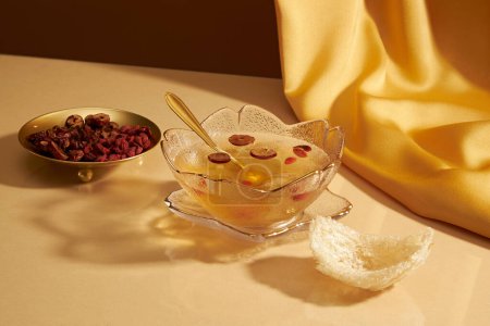 A glass transparent bowl filled with bird nest soup decorated with edible bird nest and a golden dish of dried goji berries. Bird nest can help people sleep well and reduce stress