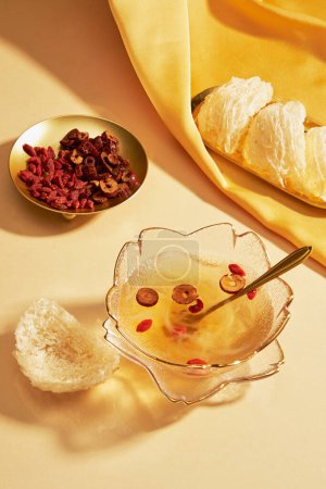 A dish of edible bird nest placed on yellow fabric, decorated with, a glass bowl of bird nest soup, a golden dish of dried goji berries and jujube. Bird nest is very well-known in Southeast Asia